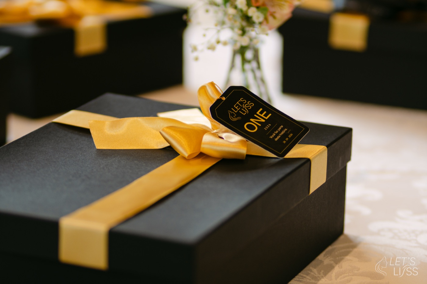 Caixa preta com laço dourado e a etiqueta do Let's Liss One
